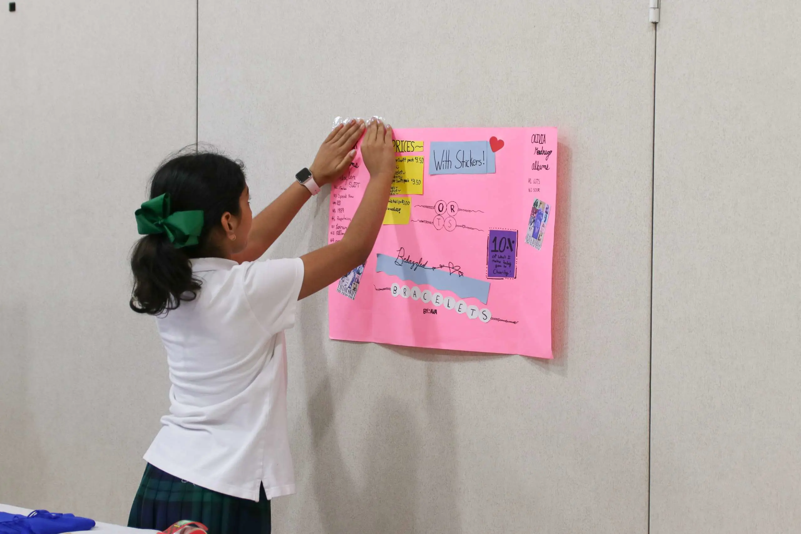 a primary student putting up a poster on a wall advertising bracelets with prices
